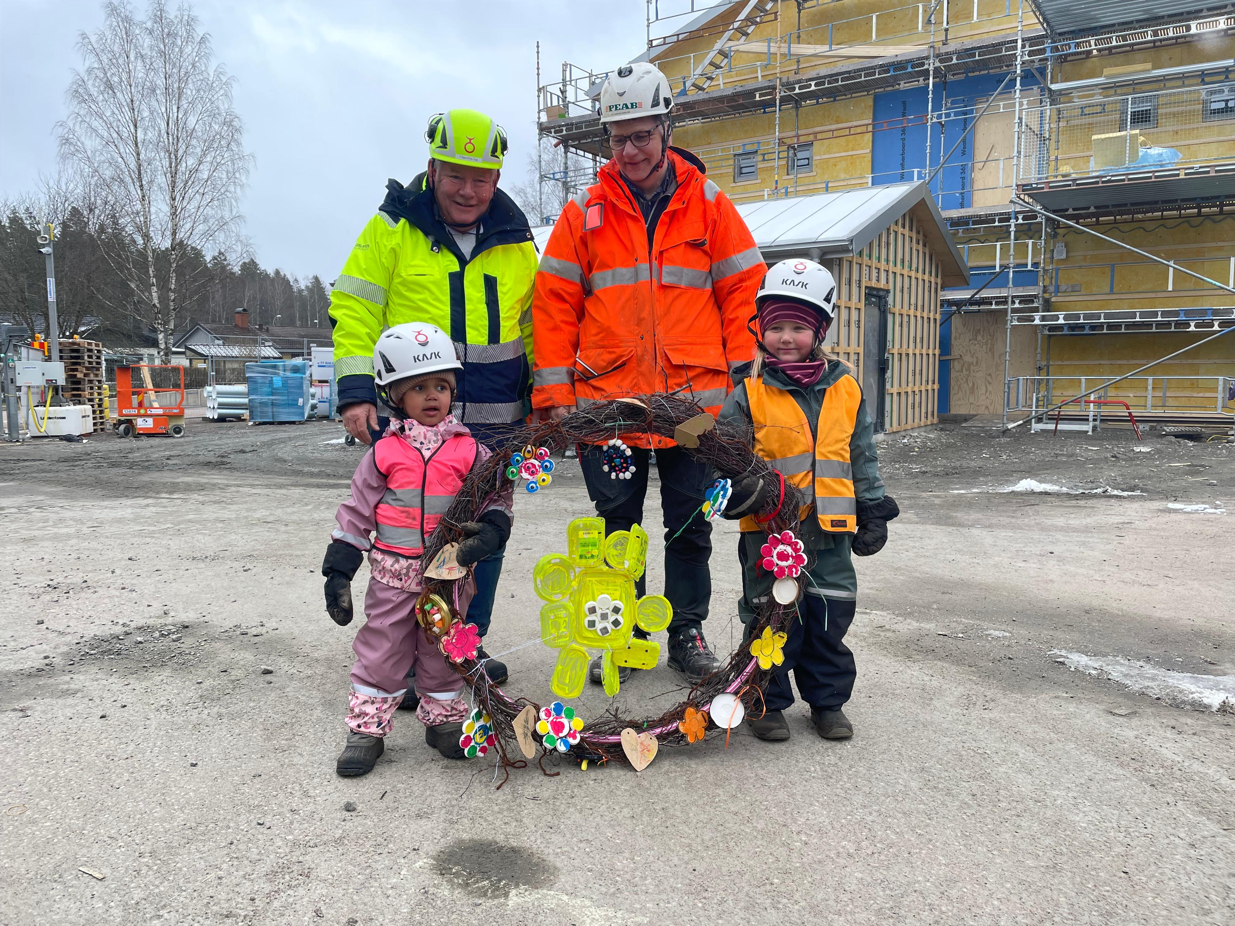Två barn, projektledare och platschef framför nybyggnationen av Sörgårdens förskola
