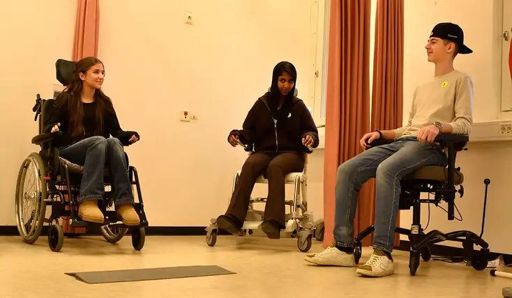 Tre ungdomar testar varsin rullstol.