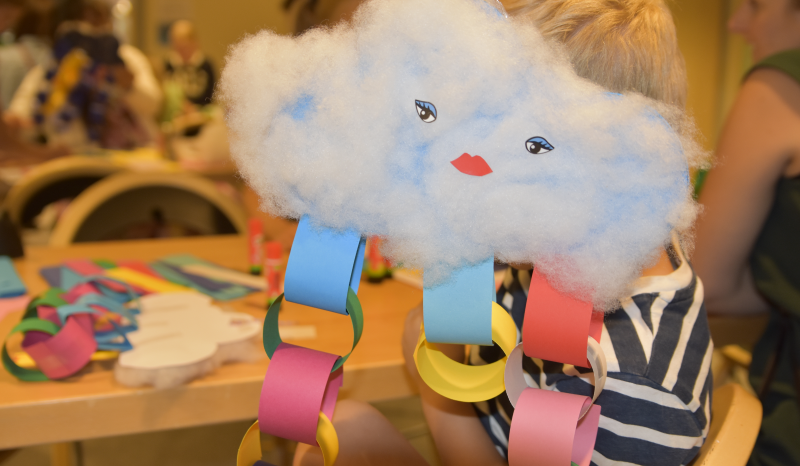 Ett moln gjort av papper och vadd. Under molnen hänger färgglada girlanger som ska föreställa blixtar.