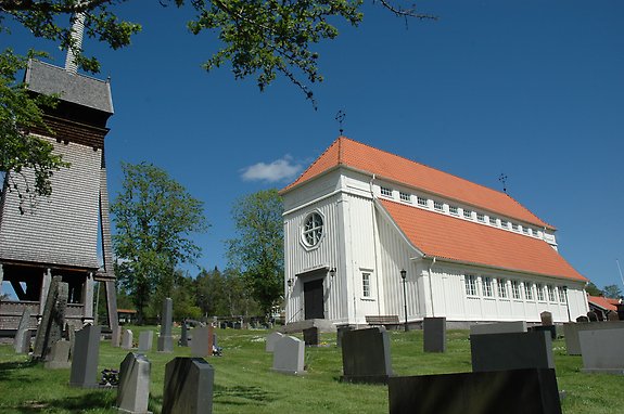 en äldre vitmålad kyrka med ett runt fönster och ett ringtorn mitt emot
