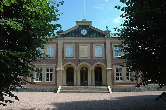 äldre stenhus med runda valv vid dörren och en klocka på tornet.