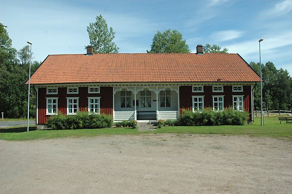en äldre skola med många fönster och en veranda på framsidan med en stor parkering framför.