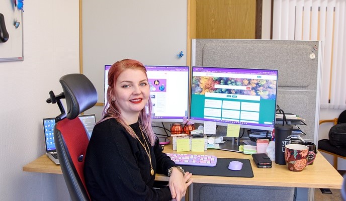 Person sitter vid skrivbord framför skärmar med Gislaveds kommuns webb