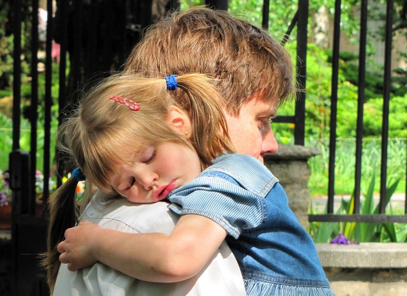 En liten flicka sover mot en mans axel.