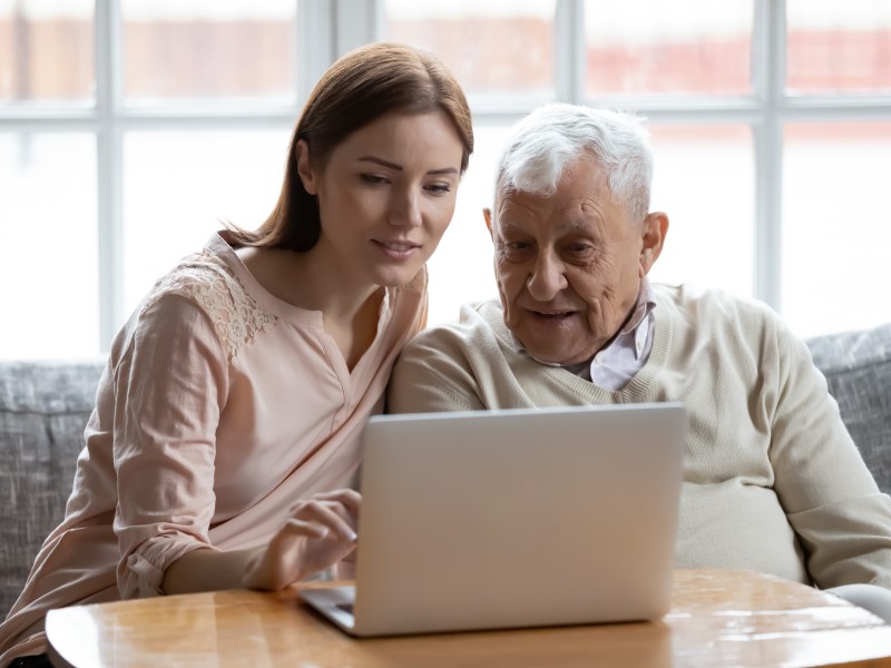 Yngre kvinna hjälper en äldre man vid datorn.