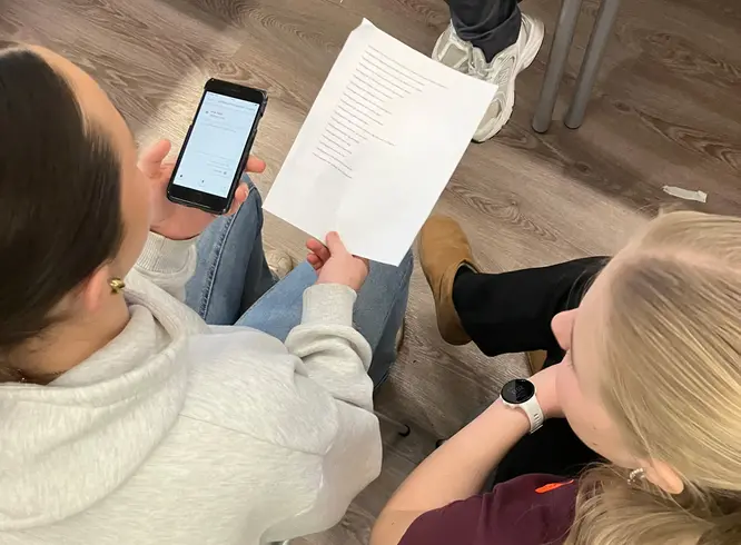 närbild på två elever som provar prata in journalanteckningar i en digital tjänst i en mobiltelefon.