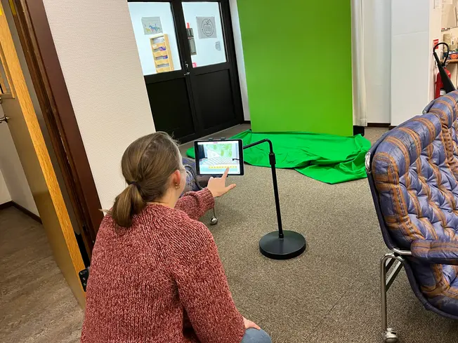 Foto på förberedelser inför ett pass med förskolan. Elida sitter på golvet och har en grön skärm framför sig.