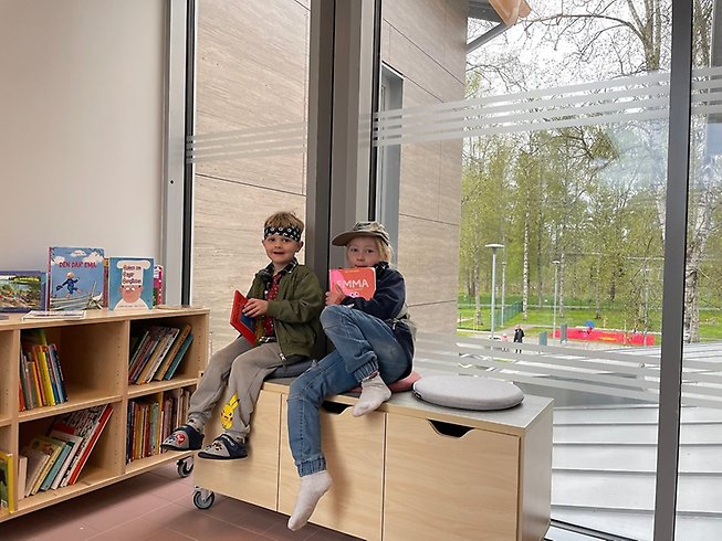 Två barn med varsin bok i handen uppkrupna på en bänk.