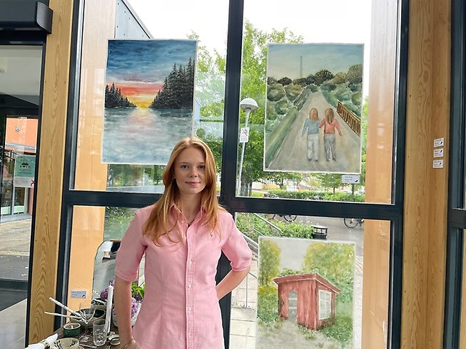 Ung kvinna framför egenmålade tavlor.