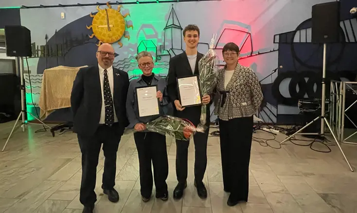 Två män och två kvinnor står på rad med blommor och diplom in händerna.