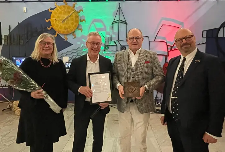 En kvinna och tre män står på rad med blommor och diplom i händerna.