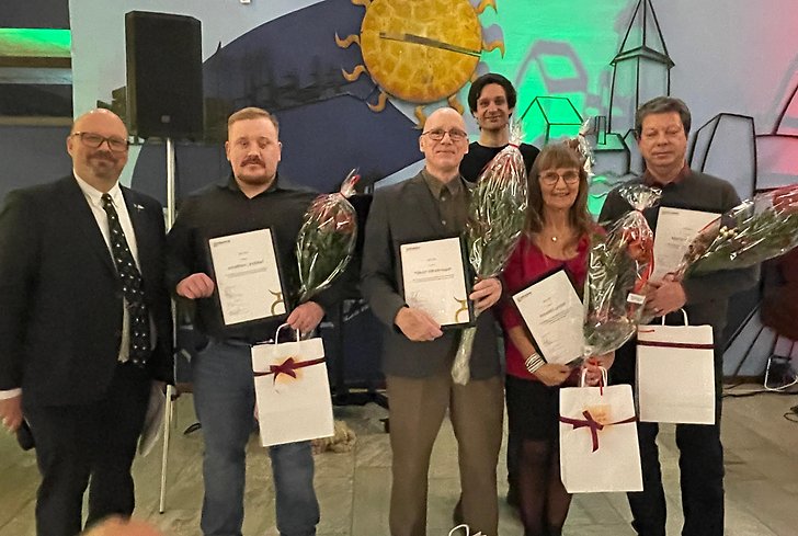 6 personer står bredvid varandra med diplom och papperskassar i händerna. 