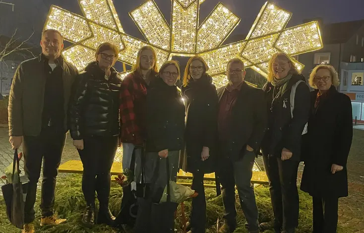 8 personer står uppradade framför en stor lysande snöflinga.