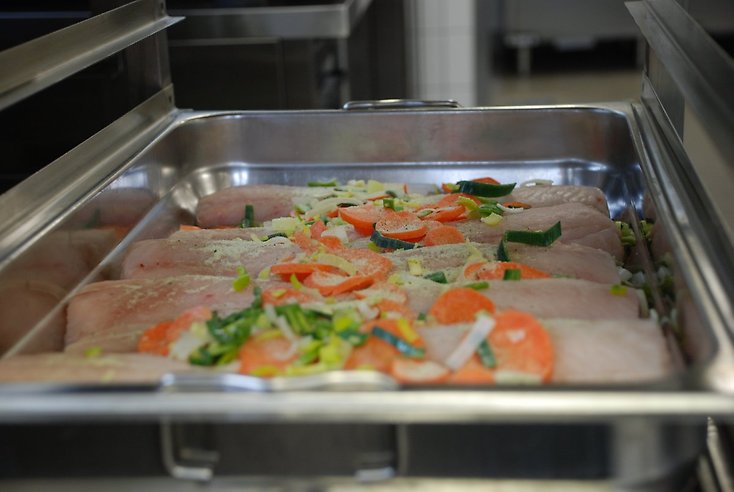 fiskfileer ligger på ett bleck. över dem har man strött olika grönsaker.