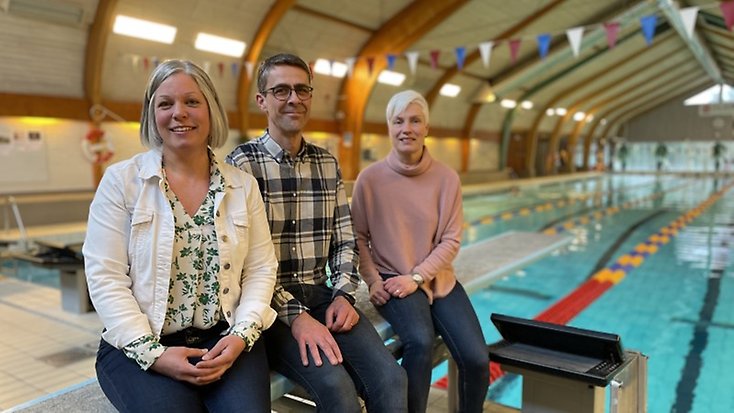 Jenny, Dan och Anna sitter på trampolinen framför simbassängen i Gislebadet.
