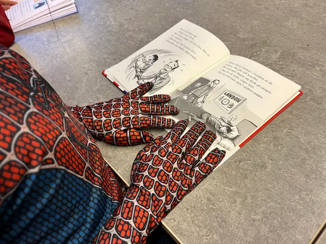 Foto på en elev som läser en bok iförd Spidermandräkt.