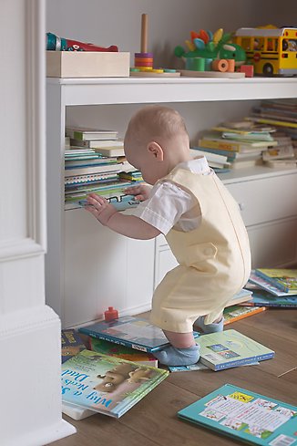 ett litet barn som står med stöd av en bokhylla