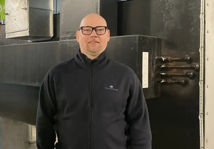 En man i svart tröja och glasögon som står i en industrimiljö.