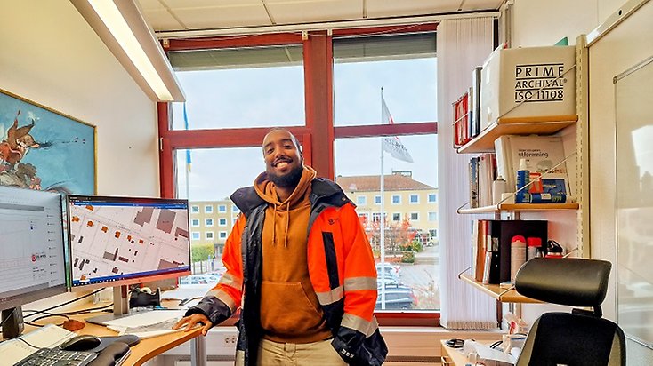 Person står i ett arbetsrum i kommunhuset med kommunens flagga i bakgrunden.