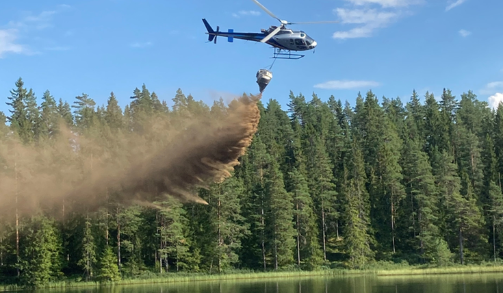 Helikopter som flyger över en sjö och släpper ut kalk. 