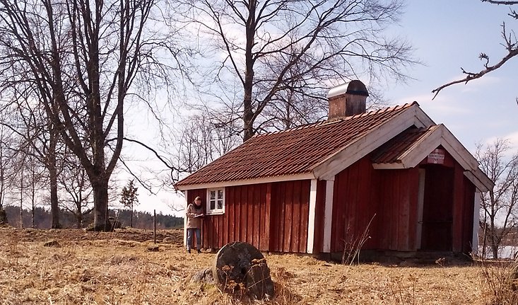 en gammal stuga med ett litet fönster på sidan liggandes på en åker.