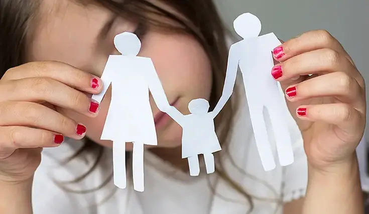 Ledsen flicka som håller i urskurna pappersfigurer som symboliserar en mamma och en pappa som håller i ett barns händer.