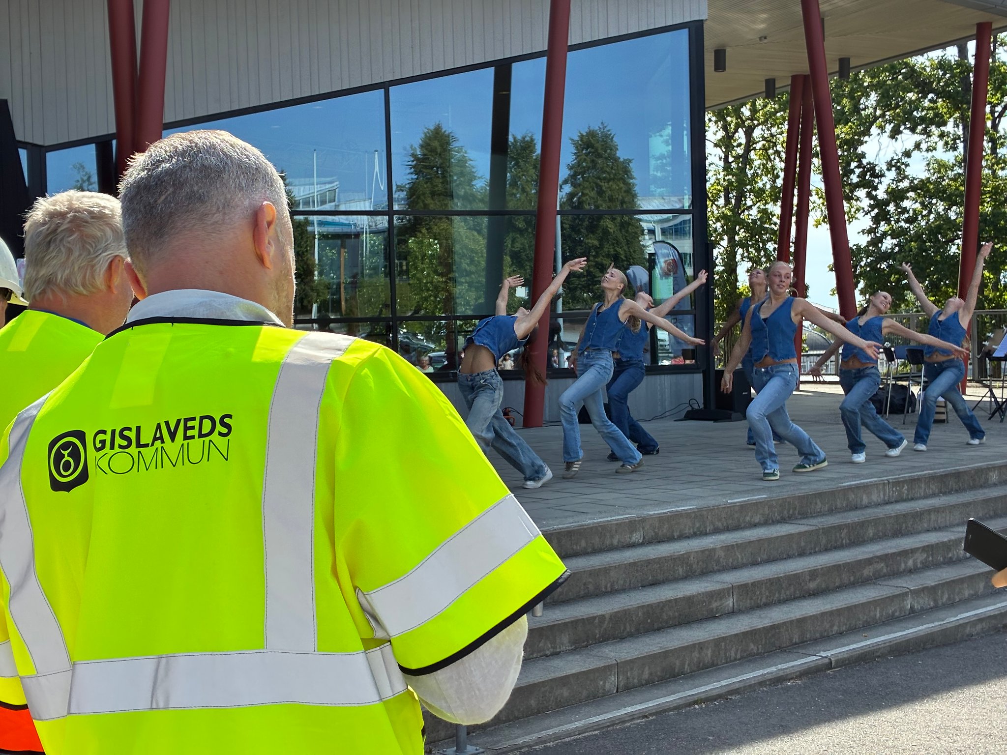 Danselever uppträder i förgrunden syns ryggen på en man med Gislaveds kommunlogga