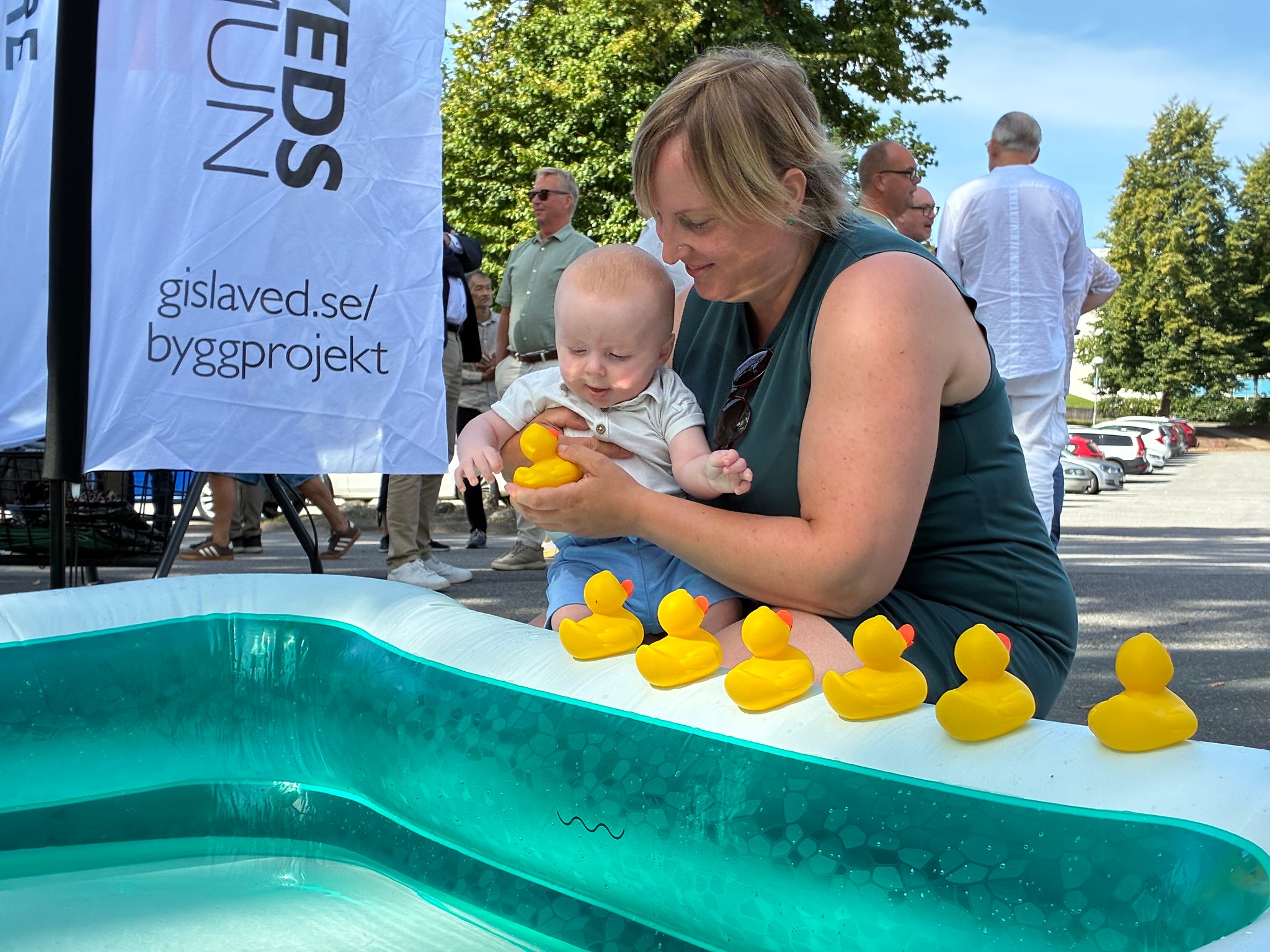 Litet barn med mamma sitter vid poolkanten och leker med badankor