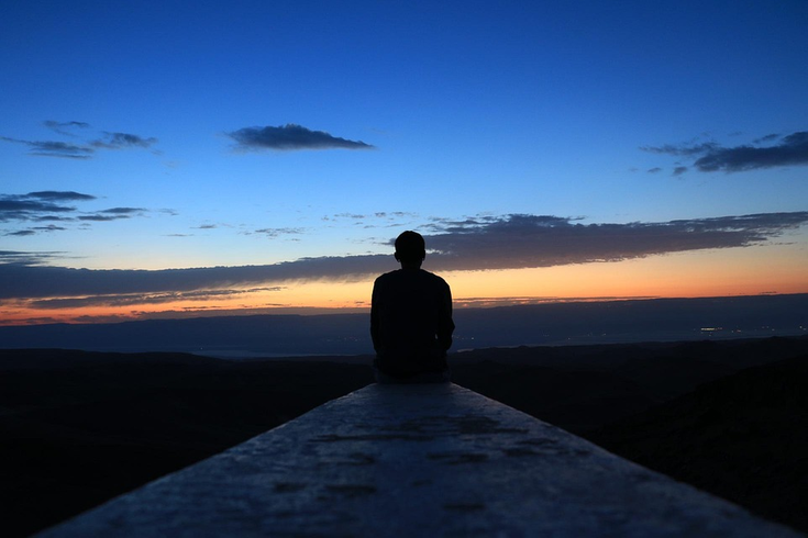 en ensam person sitter och tittar på en solnedgång.