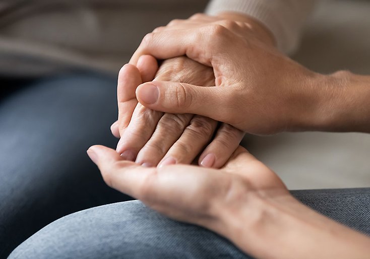 Två händer tillhörande en yngre person håller en äldre persons hand.
